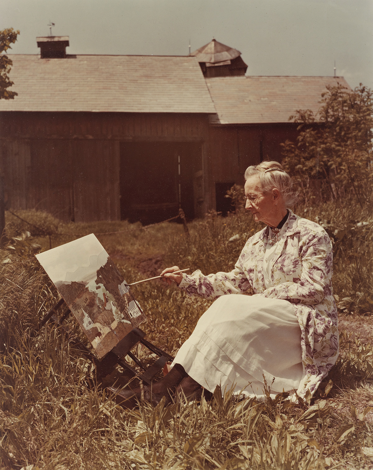 HARRY WARNECKE (1900-1984) Grandma Moses painting a scene.